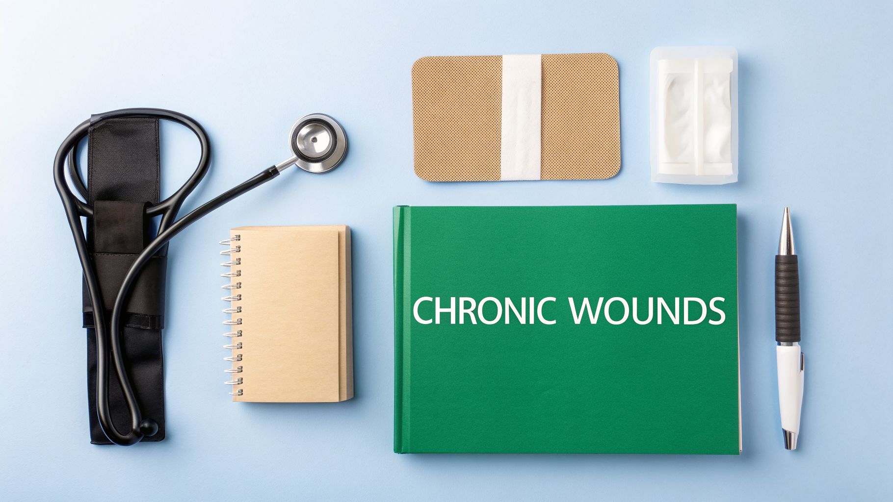 A flat lay of medical supplies including a stethoscope, notebook, pen, band-aids, and a book titled 'Chronic Wounds'.