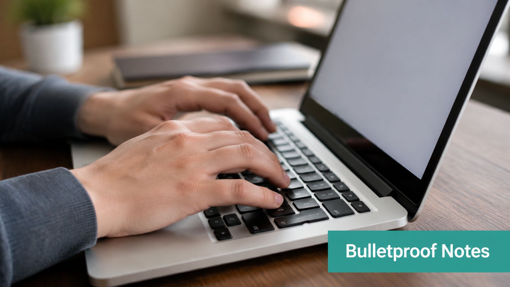 A close-up view of a person typing on a silver laptop on a wooden desk.