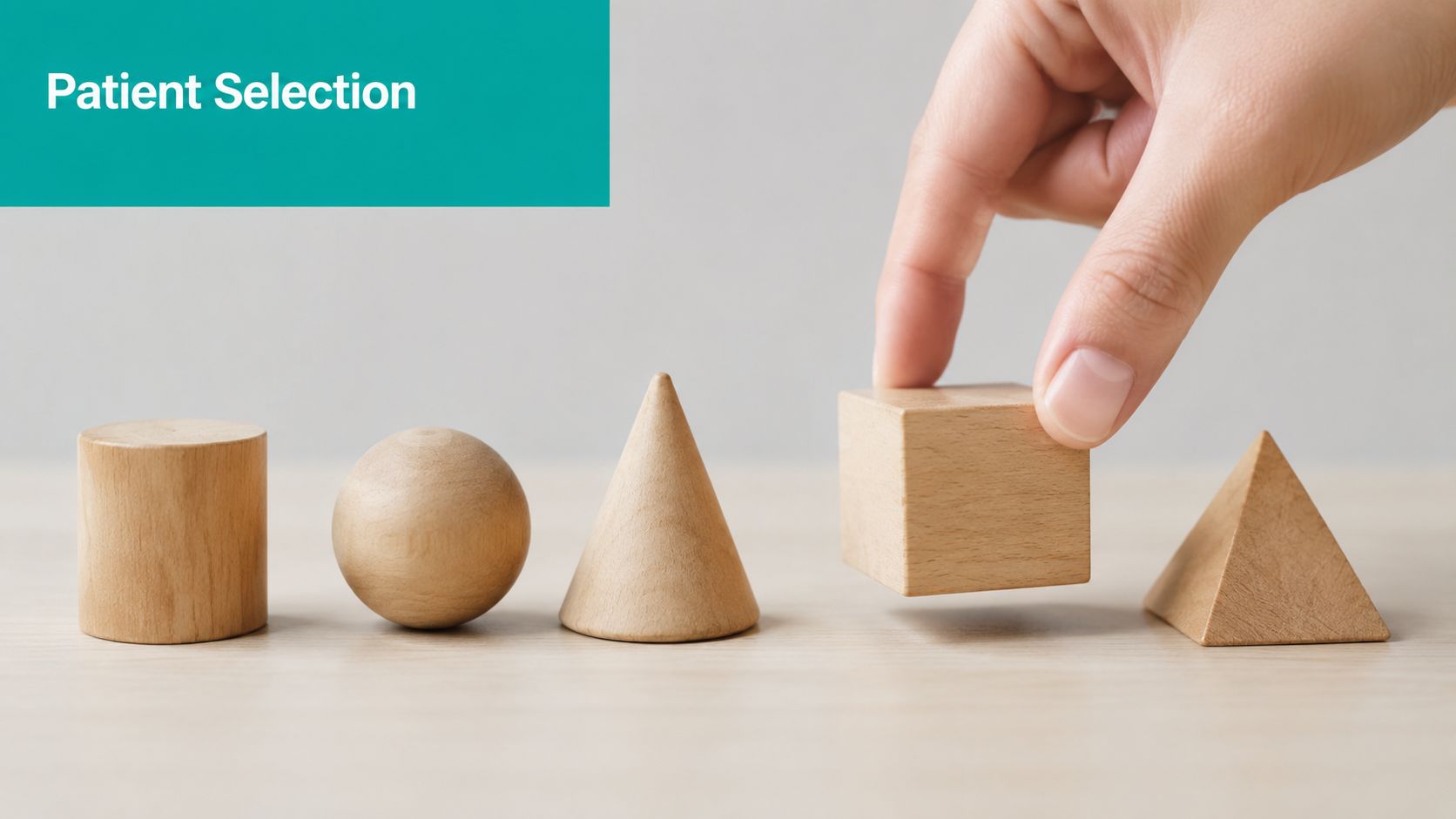 A hand selecting a wooden cube from a row of various wooden geometric shapes on a table.