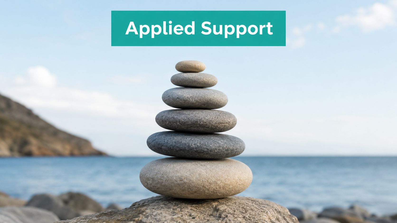 A stack of balanced smooth river stones resting on a large rock overlooking the ocean.